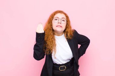 Genç kızıl saçlı kadın kapiş ya da para hareketi yapıyor, sana borçlarını ödemeni söylüyor! Pembe duvara yaslan