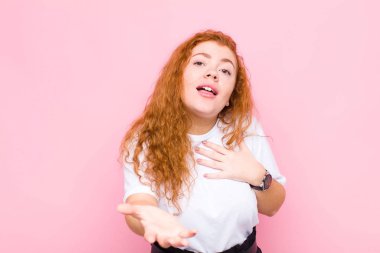 Genç kızıl saçlı kadın mutlu ve aşık, bir eli kalbinin yanında, diğeri ise pembe duvara yaslanmış.