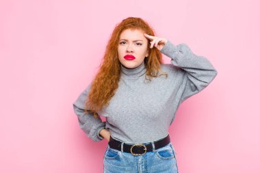 Genç kızıl saçlı kadın şaşkın ve şaşkın hissediyor. Deli, deli ya da pembe duvara karşı aklını kaçırmış olduğunu gösteriyor.