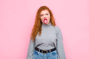 Genç kızıl saçlı kadın tiksinmiş ve rahatsız olmuş hissediyor. Dilini dışarı çıkarıyor. Pis ve iğrenç bir şeyden hoşlanmıyor.