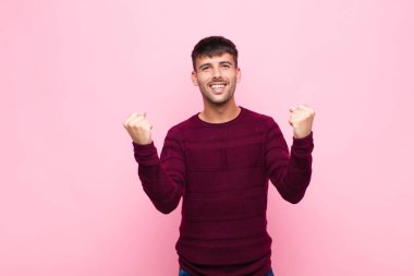 Genç ve yakışıklı bir adam inanılmaz bir başarıyı kutluyor. Kazanan gibi, heyecanlı ve mutlu görünüyor. Al bakalım! Pembe duvara yaslan