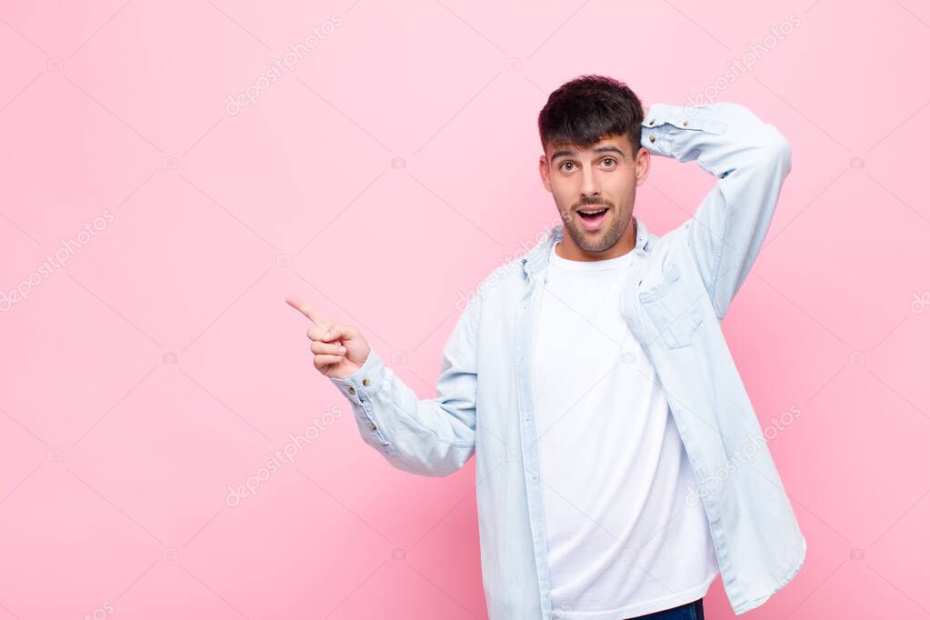 young handsome man laughing, looking happy, positive and surprised, realizing a great idea pointing to lateral copy space against pink wall