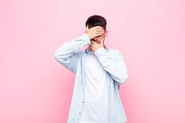 Genç yakışıklı adam kameraya hayır diyen iki eliyle yüzünü kapatıyor! Resimleri reddetmek ya da pembe duvara yaslanan fotoğrafları yasaklamak