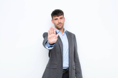 Genç yakışıklı adam ciddi, sert, hoşnutsuz ve kızgın görünüyor. Avuç içini açıp beyaz duvara karşı jestleri durduruyor.