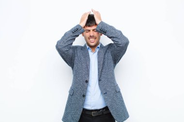 Genç yakışıklı adam stresli ve endişeli, bunalımda ve hayal kırıklığına uğramış, iki elini de beyaz duvara doğru kaldırıyor.