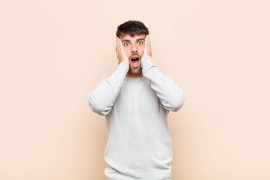 Genç yakışıklı adam hoş olmayan bir şekilde şaşırmış, korkmuş ya da endişeli görünüyor, ağzı sonuna kadar açık ve sıcak duvara karşı iki kulağını da kapatıyor.