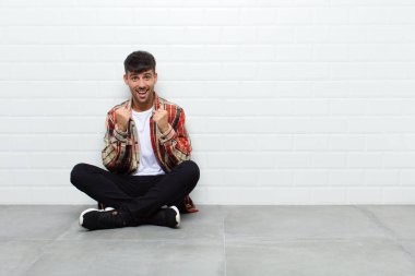 Genç yakışıklı adam şok olmuş, heyecanlı ve mutlu, gülüyor ve başarıyı kutluyor, vay canına! Beton zeminde oturuyor.