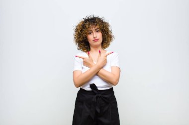 Kafası karışık, güvensiz ve beyaz duvara karşı şüpheyle zıt yönlere bakan genç ve güzel bir kadın.