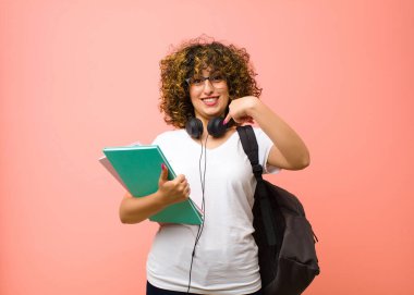 Genç ve güzel bayan öğrenci mutlu, şaşırmış ve gururlu hissediyor, pembe duvara karşı heyecanlı ve hayret dolu bir bakışla kendini işaret ediyor.