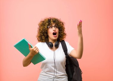 Genç, güzel bayan öğrenci kendini mutlu, şaşkın, şanslı ve şaşırmış hissediyor. Zaferi kutlarken iki elini de pembe duvara dayamış.