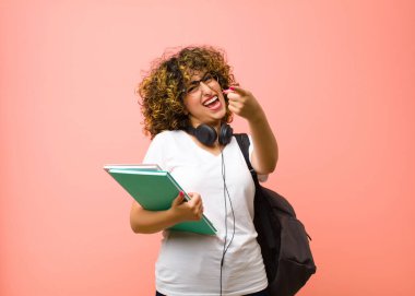 Genç, güzel bir bayan öğrenci kendini mutlu, sakin, rahat ve başarılı hissediyor, kameraya bakıyor, pembe duvara karşı seni seçiyor.