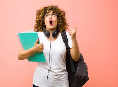 Genç ve güzel bir kız öğrenci. Huşu içinde ve ağzı açık. Pembe duvara karşı şaşkın ve şaşkın bir bakışla yukarıya bakıyor.