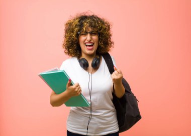 Genç, güzel bir bayan öğrenci zafer çığlıkları atıyor, gülüyor, mutlu ve heyecanlı hissediyor pembe duvara karşı başarıyı kutlarken.