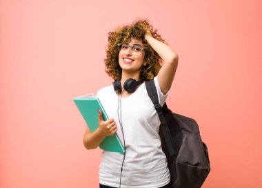 Genç ve güzel bir bayan öğrenci neşeli ve tesadüfen gülümsüyor, pembe duvara karşı pozitif, mutlu ve kendinden emin bir bakışla yumruk yumruğa bakıyor.