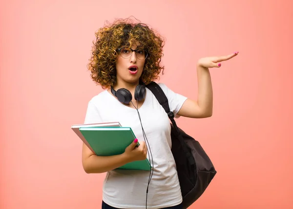 側のコピースペースに両手でオブジェクトを保持している若いかなり学生の女性は ピンクの壁に対してオブジェクトを表示 提供または広告 — ストック写真