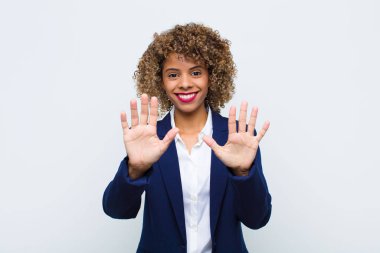 Afro-Amerikan genç bayan gülümsüyor ve arkadaş canlısı görünüyor, onuncu ya da onuncu numarayı gösteriyor, düz duvara doğru sayıyor.