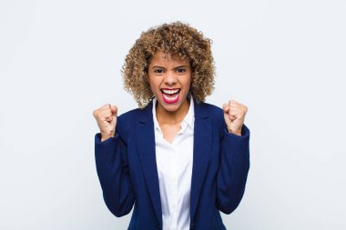 Genç Afrikalı Amerikalı kadın mutlu, şaşırmış ve gururlu, bağırıyor ve başarıyı büyük bir gülümsemeyle kutluyor.