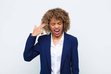 Genç Afro-Amerikan kadın mutsuz ve stresli görünüyor, intihar jesti elle silah işareti yapıyor, düz duvara doğru işaret ediyor.