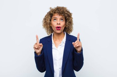 Afro-Amerikalı genç bir kadın hayranlık duyuyor ve ağzı açık. Düz duvara karşı şaşkın ve şaşkın bir bakışla yukarıya bakıyor.