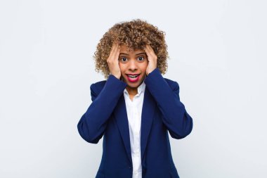 Afro-Amerikan görünümlü genç bir kadın hoşnutsuz, korkmuş ya da endişeli görünüyor, ağzı sonuna kadar açık ve iki kulağı da düz duvara karşı kapalı.