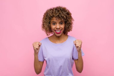 Genç Afrikalı Amerikalı kadın şok olmuş, heyecanlı ve mutlu hissediyor, gülüyor ve başarıyı kutluyor, vay canına! Pembe duvara yaslan