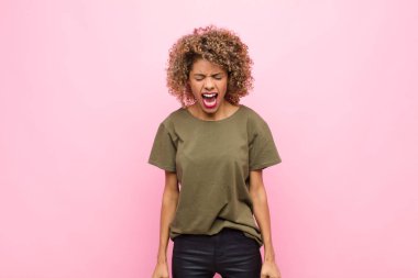 Genç Afrikalı Amerikalı kadın agresif bir şekilde bağırıyor, çok kızgın, sinirli, öfkeli ya da sinirli görünüyor, pembe duvara karşı hayır diye bağırıyor.