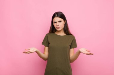 Genç, güzel bir kadın kendini cahil ve şaşkın hissediyor. Hangi seçeneği seçeceğinden emin değil. Pembe duvara karşı merak içinde.