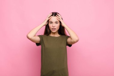 Genç, güzel bir kadın dehşete kapılmış ve şok olmuş hissediyor. Pembe duvara karşı yapılan bir hata karşısında ellerini kaldırıyor ve panikliyor.