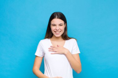 Genç ve güzel bir kadın komik bir şakaya yüksek sesle gülüyor, mutlu ve neşeli hissediyor, mavi duvara karşı eğleniyor.