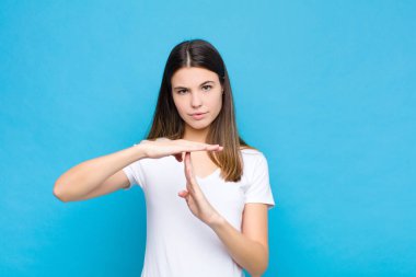 Genç, güzel bir kadın ciddi, sert, kızgın ve hoşnutsuz görünüyor. Mavi duvara karşı mola işareti yapıyor.