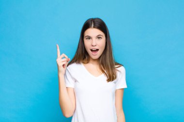 Genç ve güzel bir kadın bir fikri fark ettikten sonra mutlu ve heyecanlı bir dahi gibi hissediyor, neşeli bir şekilde parmağını kaldırıyor, eureka! mavi duvara yaslan