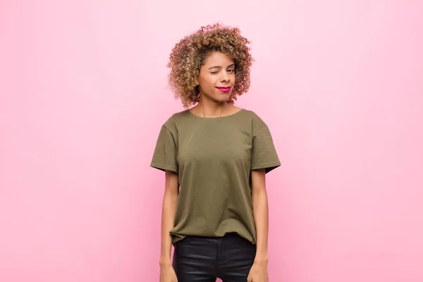 若いアフリカ系アメリカ人女性がピンクの壁に対して積極的な態度であなたを見て笑顔とウィンク — ストック写真