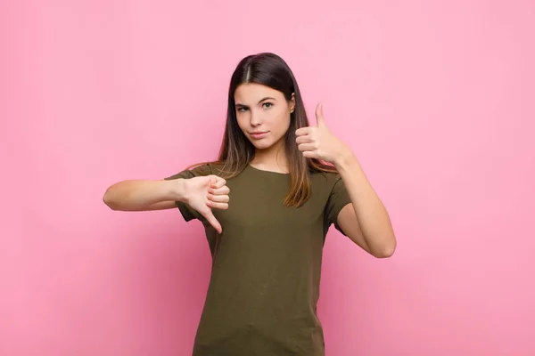 若い女性は混乱し 混乱し 自信を失い 異なるオプションやピンクの壁に対する選択で良いと悪い重み付け — ストック写真