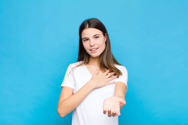 幸せそうな若い女性が手を心の隣に笑顔でもう一方は青い壁に向かって前に伸び — ストック写真