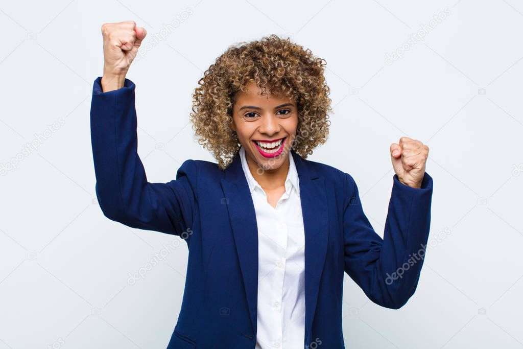 young woman african american shouting triumphantly, looking like excited, happy and surprised winner, celebrating against flat wall