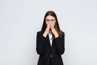 Genç iş kadını mutlu, neşeli, şanslı ve şaşırmış görünüyor. İki eli de beyaz duvara dayalı.