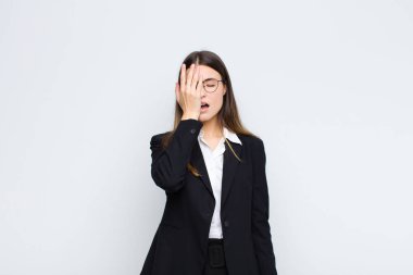 Genç iş kadını uykulu görünüyor, sıkılmış ve esniyor, baş ağrısı ve yüzünün yarısını beyaz duvarla kaplıyor.