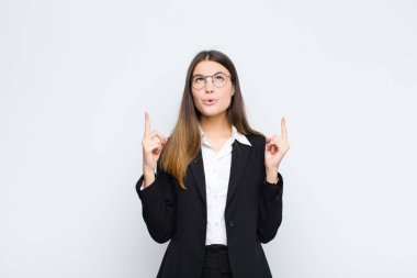 Genç iş kadını huşu ve açık ağızla beyaz duvara karşı şaşkın ve şaşkın bir bakışla yukarıya bakıyor.