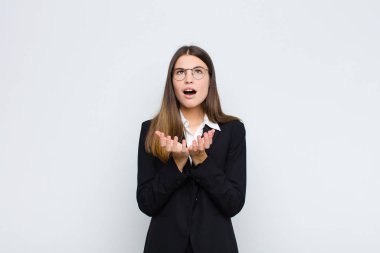 Genç iş kadını umutsuz ve hayal kırıklığına uğramış görünüyor, stresli, mutsuz ve sinirli, beyaz duvara karşı bağırıyor ve çığlık atıyor.