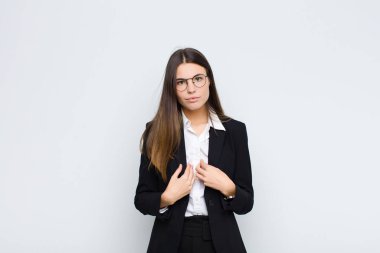 Genç iş kadını, kafası karışmış ve tuhaf bir bakışla kendini işaret ediyor. Beyaz duvara karşı seçildiği için şaşırmış ve şaşırmış.