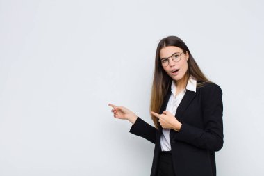 Genç iş kadını şaşkınlık ve şaşkınlık içinde, beyaz duvara karşı hayret dolu, ağzı açık bir bakışla fotokopi alanını işaret ediyor.