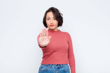 Genç ve güzel bir kadın ciddi, sert, hoşnutsuz ve kızgın görünüyor. Avuç içini açıp beyaz duvara karşı jest yapıyor.