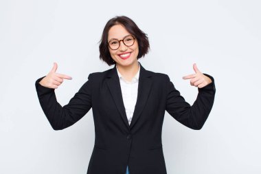 Genç iş kadını gururlu, kibirli, mutlu, şaşırmış ve tatmin olmuş görünüyor, kendini gösteriyor, beyaz duvara karşı kazanan gibi hissediyor.