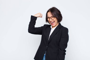 Genç iş kadını kendini mutlu, memnun ve güçlü hissediyor, kaslı ve formda, spor salonundan sonra beyaz duvara karşı güçlü görünüyor.