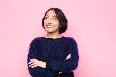 Genç, güzel bir kadın kendini mutlu, gururlu ve umutlu hissediyor, merak ediyor ya da düşünüyor, pembe duvara yaslanmış çapraz kollarıyla uzayın fotokopisini çekmek istiyor.