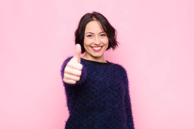 Genç, güzel bir kadın gururlu, kaygısız, kendinden emin ve mutlu, pembe duvara yaslanmış olumlu gülümsüyor.