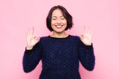 Genç ve güzel bir kadın konsantre olmuş ve meditasyon yapıyor. Tatmin olmuş ve rahatlamış hissediyor. Pembe duvara karşı bir seçim yapıyor.