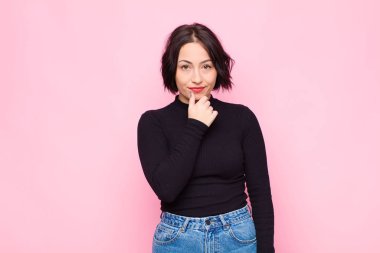 Genç, güzel bir kadın ciddi, kafası karışmış, kararsız ve düşünceli görünüyor. Seçenekler arasında veya pembe duvara karşı seçimler yapıyor.