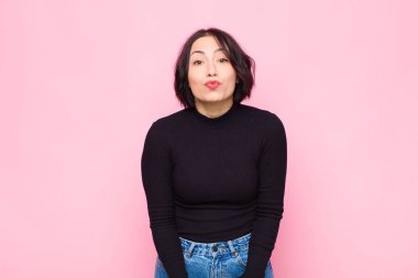 Genç, güzel bir kadın dudaklarını birbirine bastırıyor, sevimli, eğlenceli, mutlu, sevimli bir yüz ifadesiyle, pembe duvara bir öpücük yolluyor.