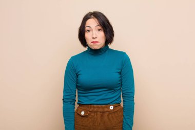 Genç, güzel bir kadın üzgün ve stresli. Kötü bir sürpriz yüzünden üzgün. Bej rengi duvara karşı olumsuz ve endişeli bir bakışla.